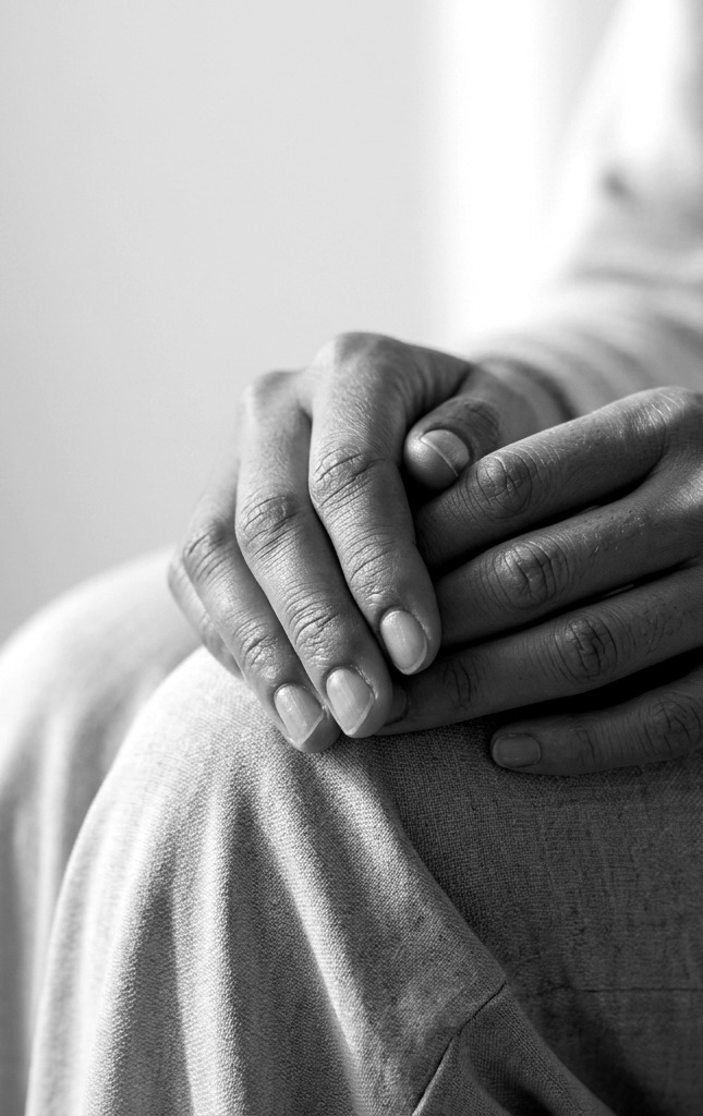 Two hands resting gently on a knee, one over the other, in soft side light.
